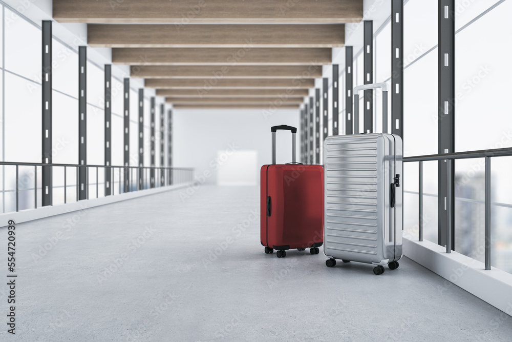红色和灰色行李箱放在现代模糊的机场内部，可以看到全景窗户和城市景观