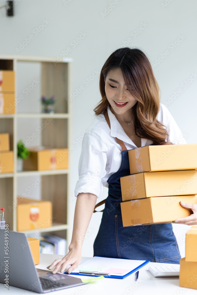 Young Asian woman start up business owner sales, working on laptop and cardboard boxes to prepare or