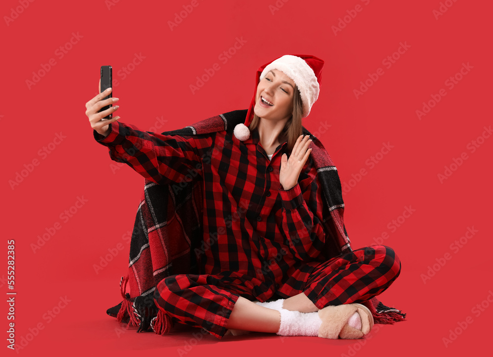 年轻女子穿着圣诞睡衣，拿着手机在红底自拍