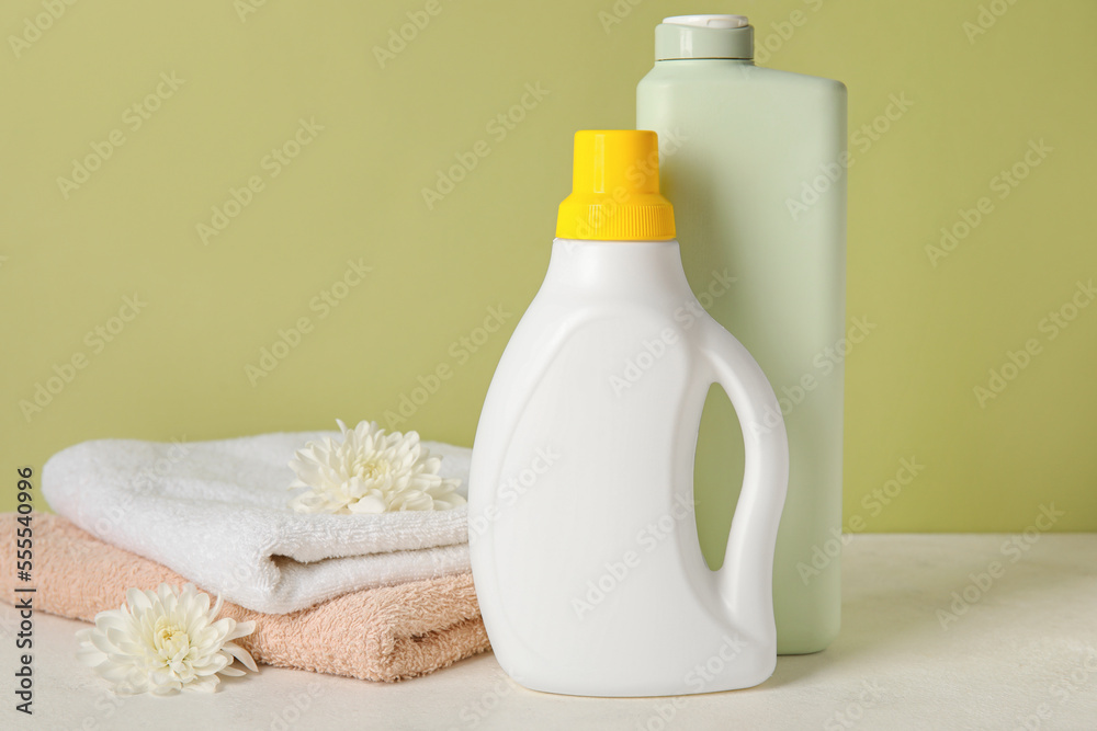 Laundry detergents and towels with beautiful flowers on table against green background