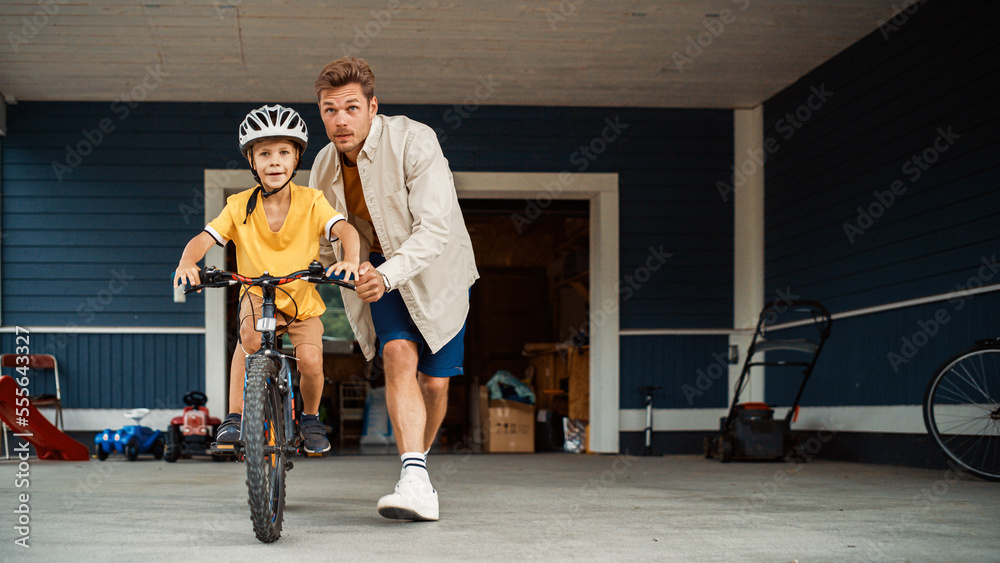 快乐的父亲在他们美丽住宅的前院教儿子骑自行车