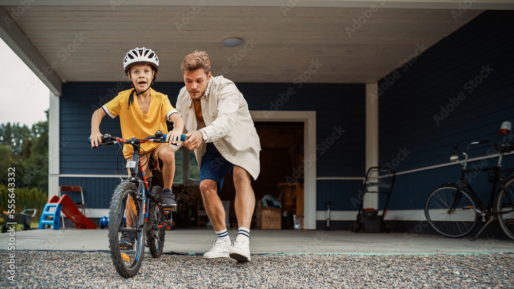 年轻的父亲在他们大住宅区的草坪上教儿子骑自行车。成功