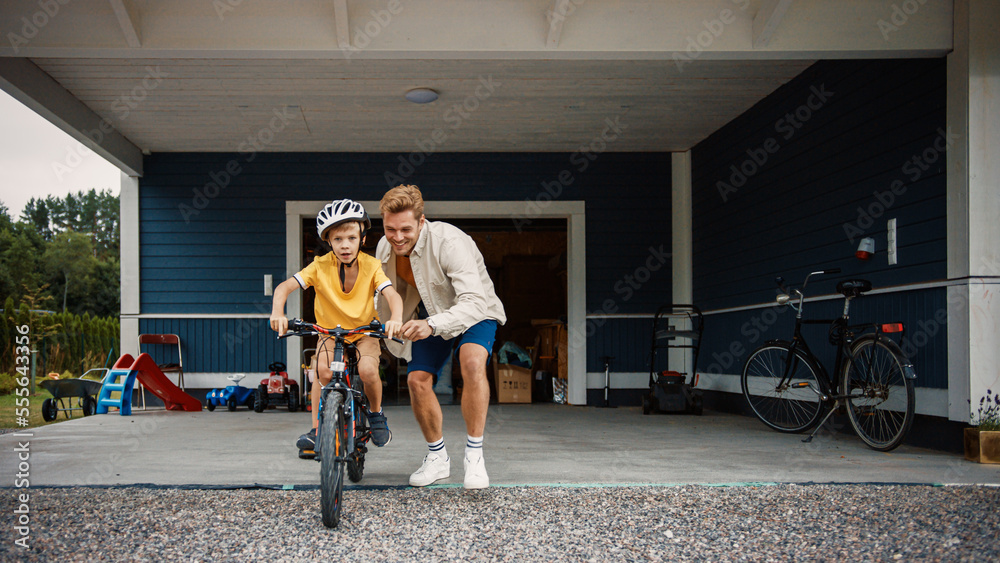 年轻的父亲在他们大住宅区的草坪上教儿子骑自行车。成功了
