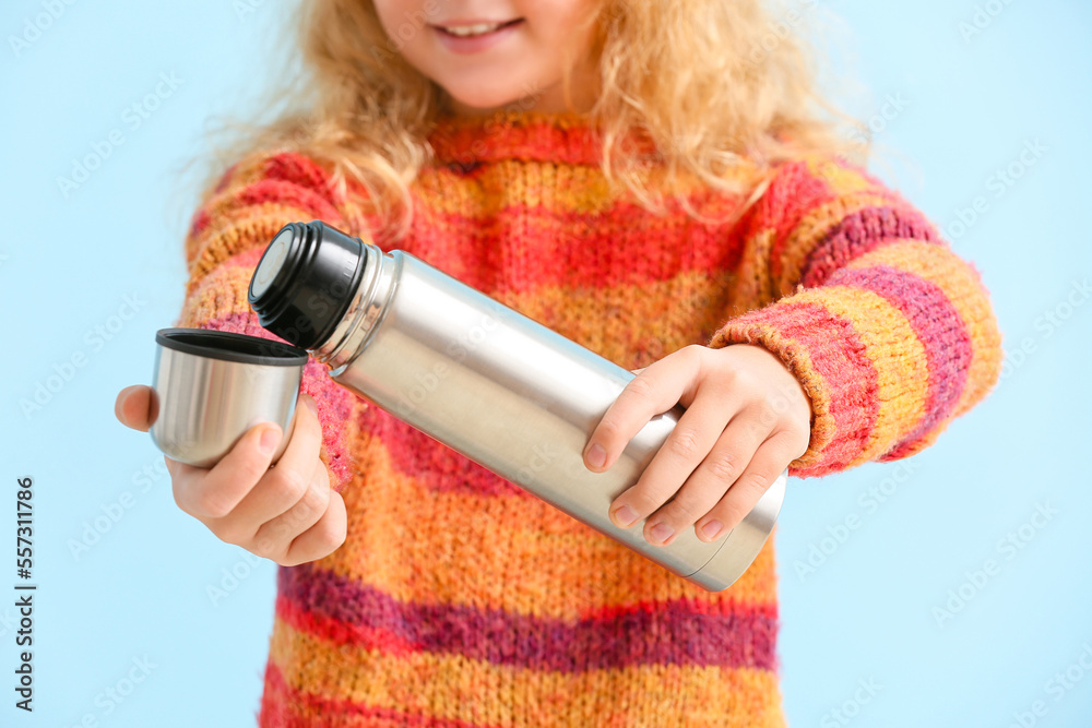 Little redhead girl with thermos on blue background, closeup