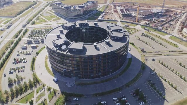 Circular office building with parking area near construction site aerial view. Stylish architectural ideas for city