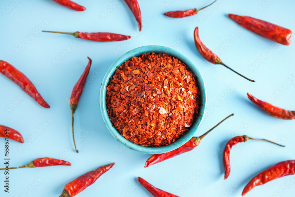Bowl of chipotle chili flakes and dried jalapeno peppers on color background