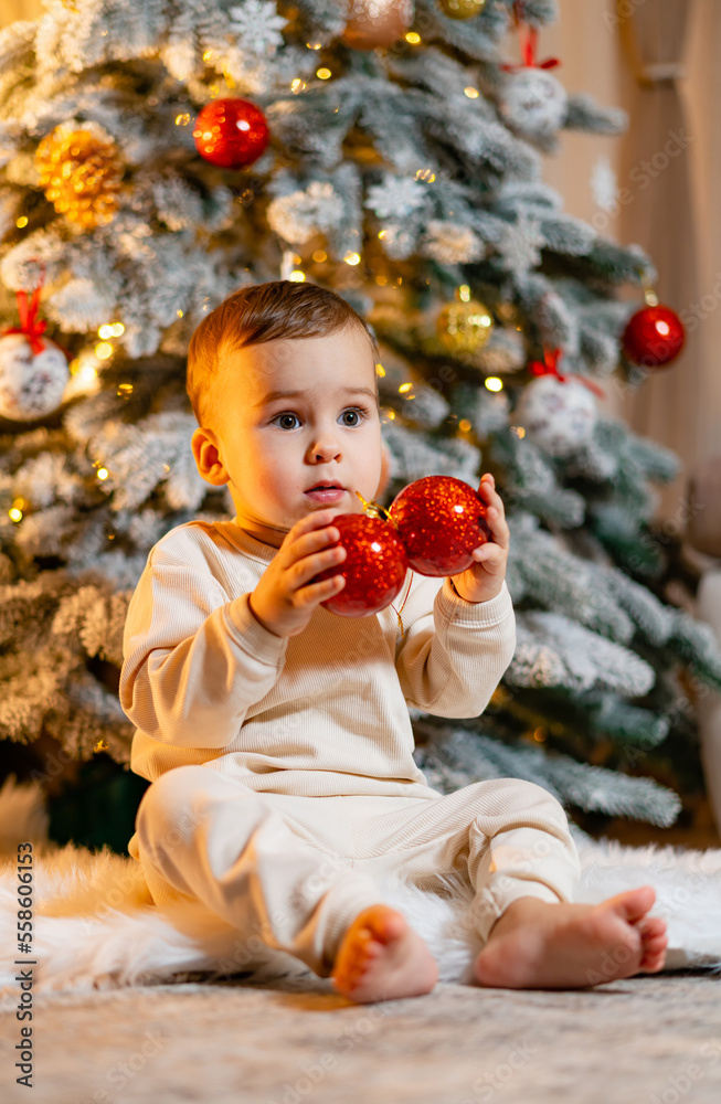 快乐的蹒跚学步的小男孩在圣诞树旁玩耍。圣诞快乐，节日快乐！