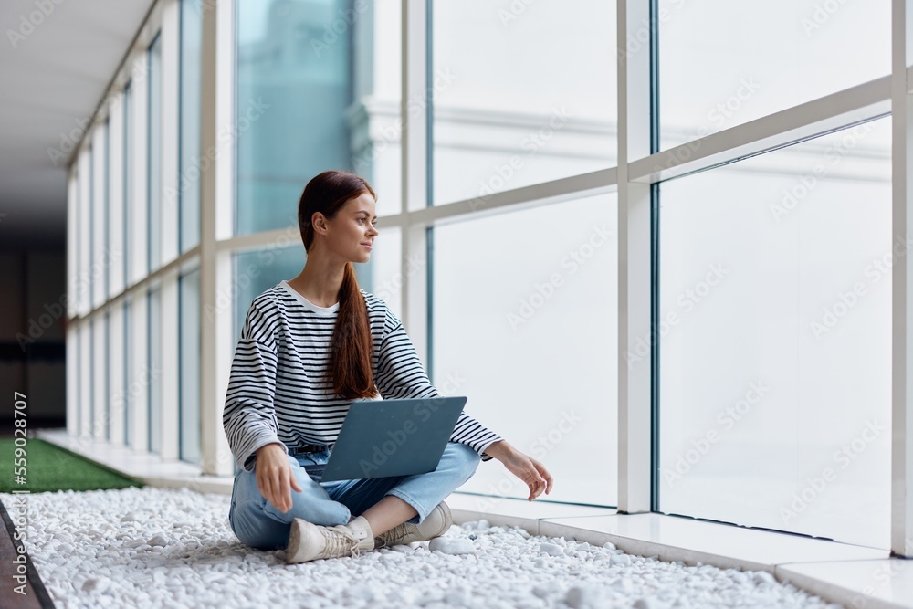 一位女性自由职业者拿着笔记本电脑坐在俯瞰城市的窗户旁，在网上订购商品