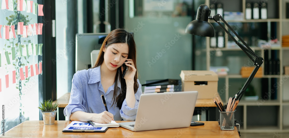亚洲商务女性坐在办公室里微笑着打电话和使用笔记本电脑。