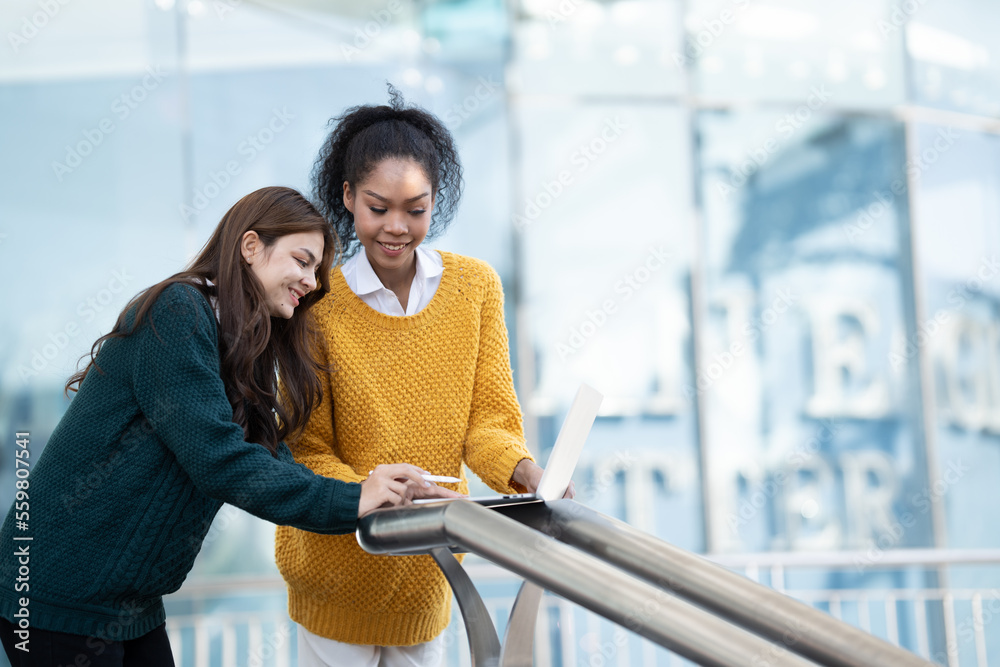 Group of two happy multiethnic friends looking at computer tablet. Portrait of young women of differ