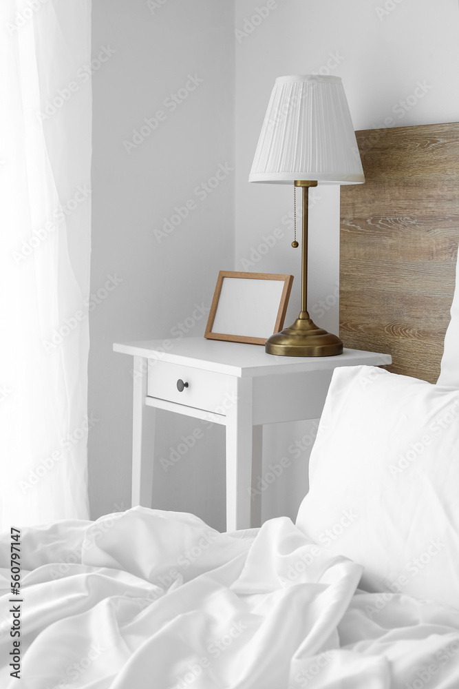 Blank photo frame and lamp on table in light bedroom