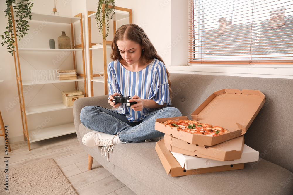 年轻女子在家玩电子游戏，手里拿着美味的披萨