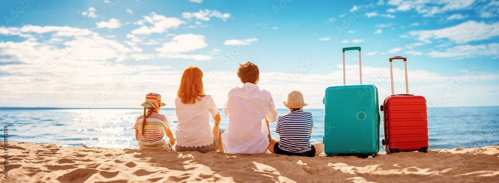 母亲和父亲带着孩子坐在海滩上，提着行李箱。