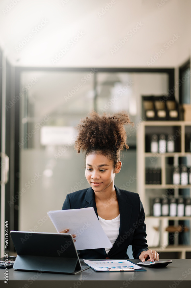 年轻漂亮的女人坐在办公桌上用平板电脑和笔记本电脑打字