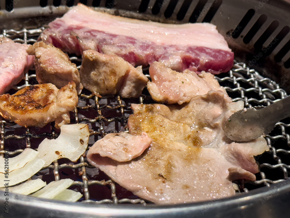 Grilling pork belly meat on a round BBQ net in restaurant for eating.
