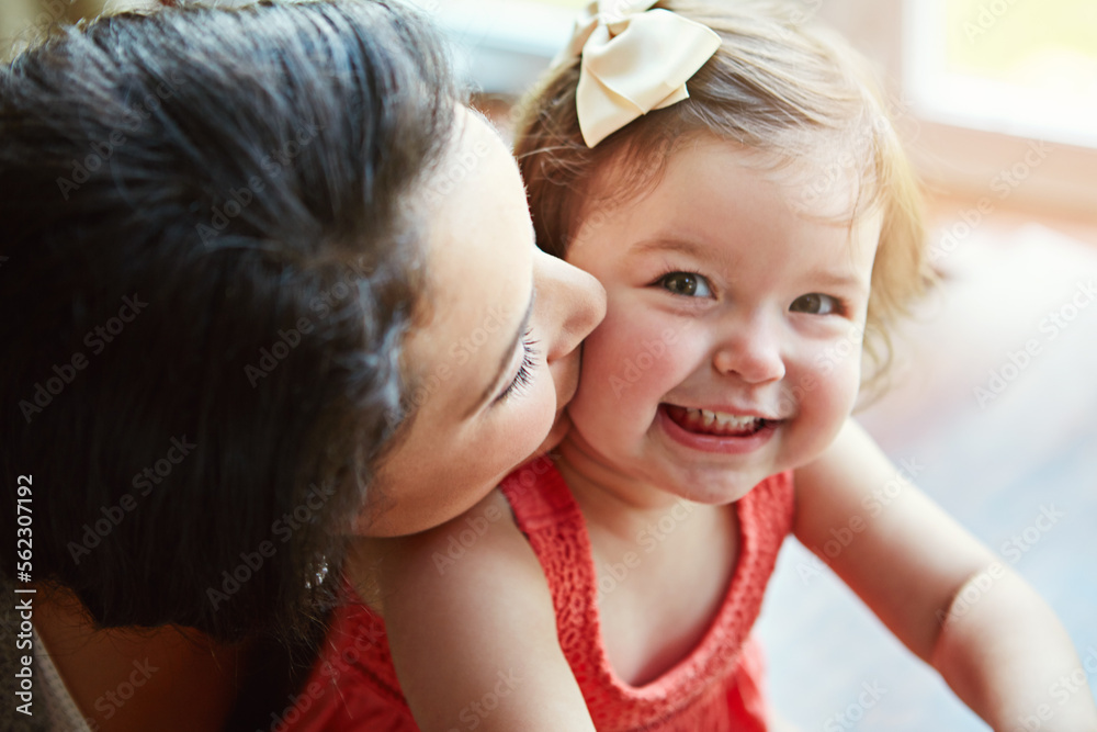 Portrait of a baby with her mother kissing her cheek while playing, bonding and spending time togeth