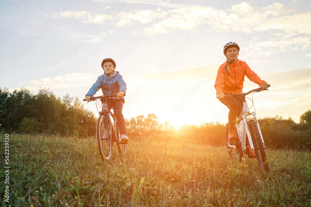 Mother and son ride a bike. Happy cute boy in helmet learn to riding a bike in park on green meadow 