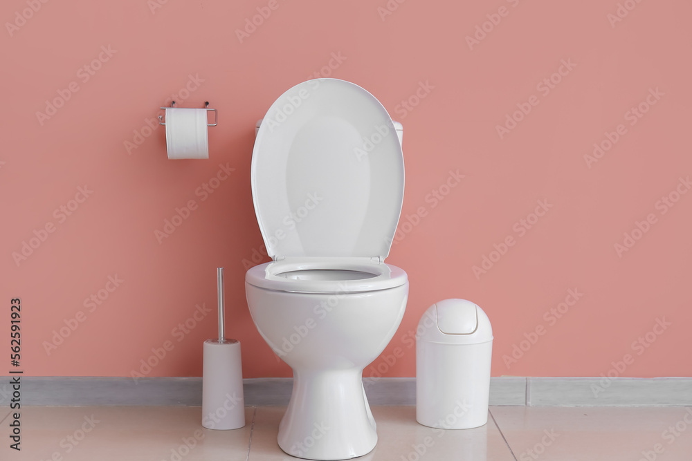 Ceramic toilet bowl, bin and paper rolls near pink wall