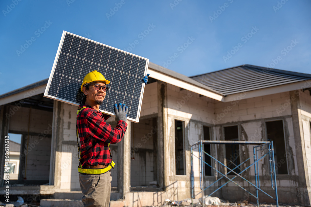 Asian technician carrying solar panels happily smiling in front of unfinished house at construction 