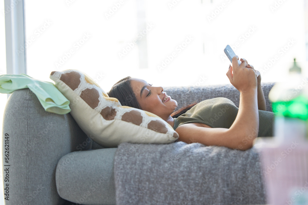 Indian woman, phone and relax happy on sofa for social media, online communication and streaming vid