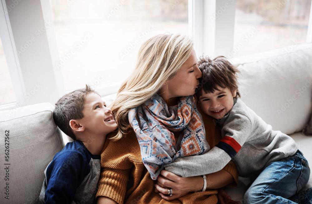 幸福的家庭，一起坐在家里客厅的沙发上，妈妈给孩子们拥抱和亲吻。