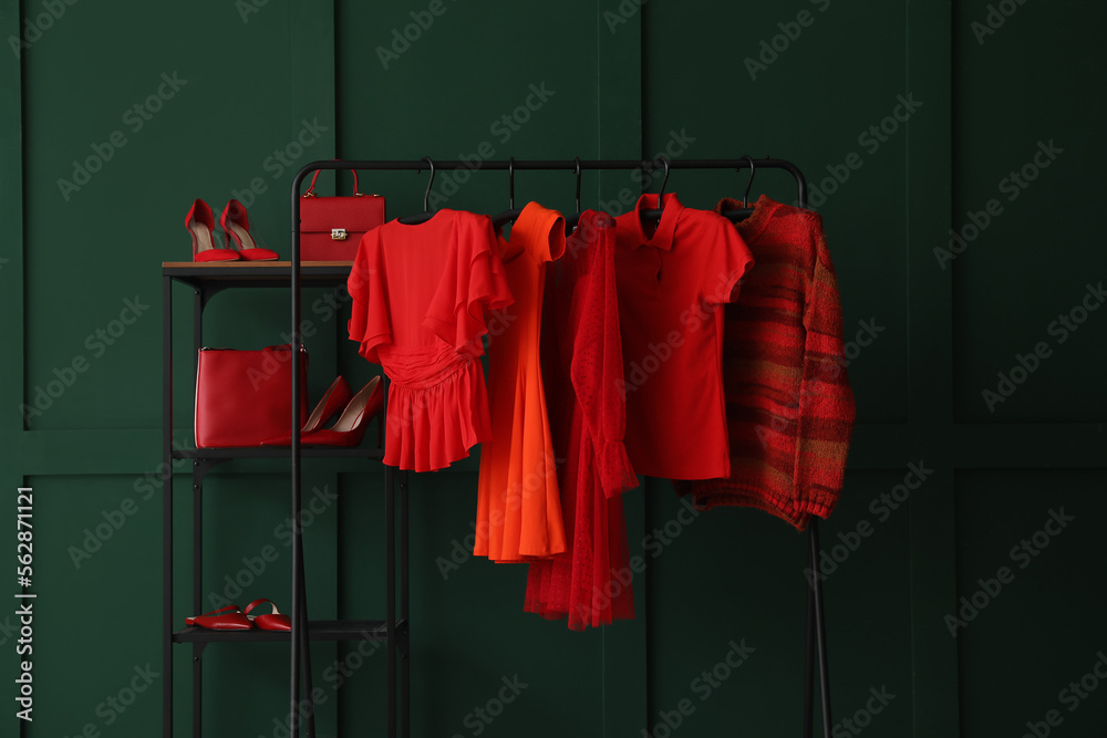 Rack with red female clothes, shelving unit and shoes near green wall