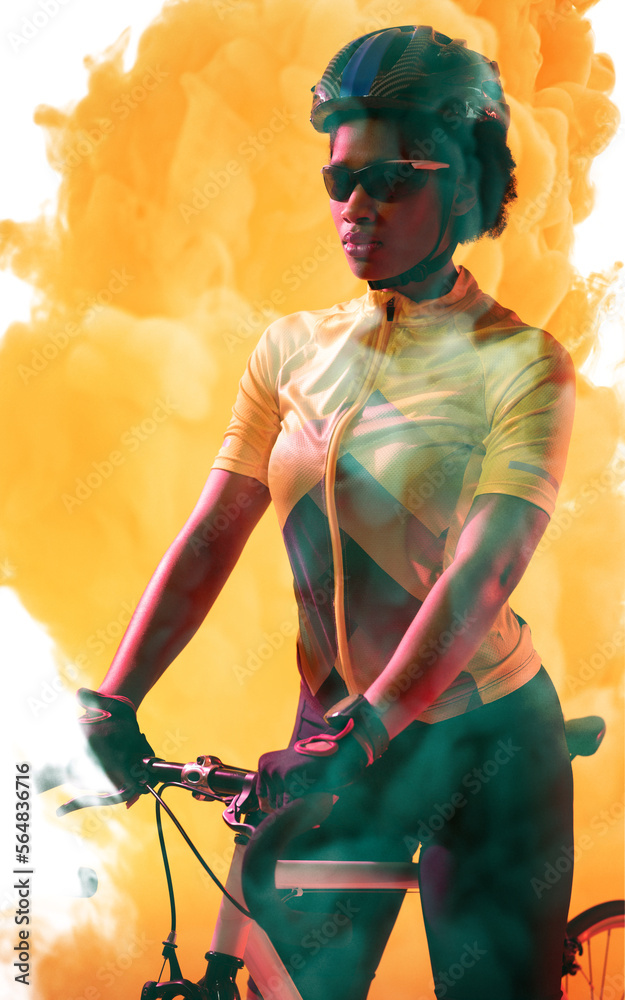 自信的非裔美国自行车手戴着头盔和眼镜，在烟雾弥漫的背景下与自行车站在一起