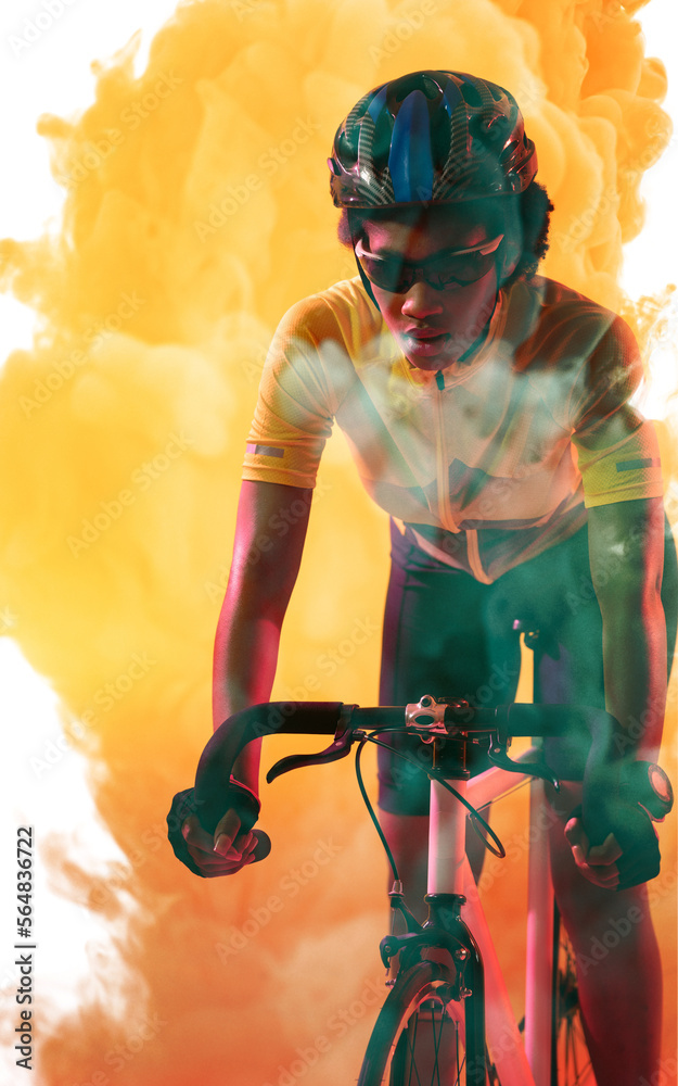 戴着头盔和眼镜的非裔美国女运动员在黄色烟雾背景下骑自行车