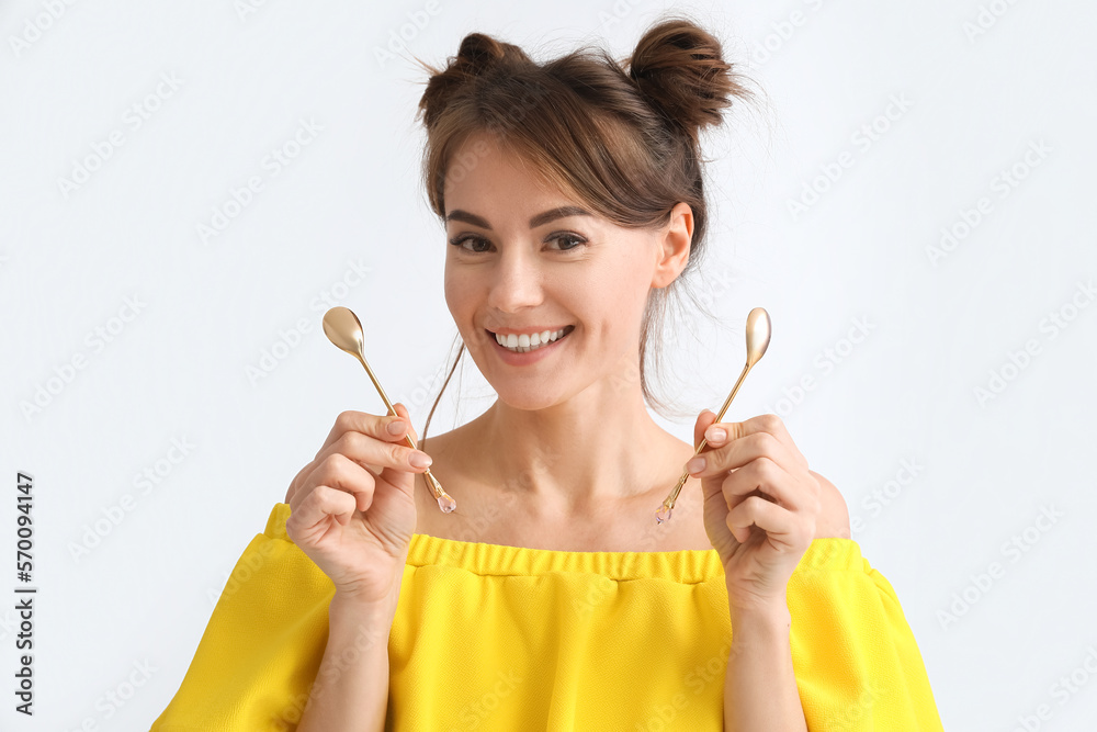 Beautiful woman with golden teaspoons on light background, closeup