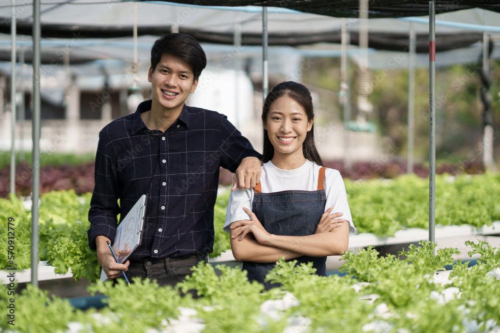 Portrait of young confident Asian farm worker standing in the green sala hydroponic farm together.