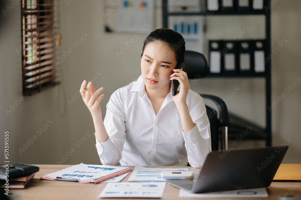 Business asian woman Talking on the phone and using a laptop with a smile while sitting at office..