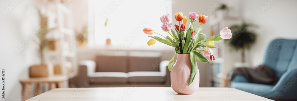 A bunch of tulips in pink vase standing on the wooden table indoors.