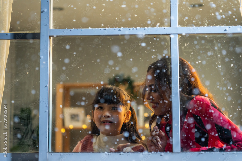 Adorable child looking at the window and admire snowflakes with mother