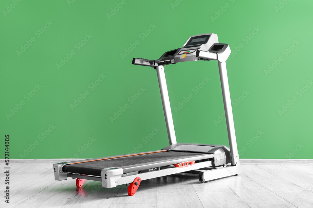 Modern treadmill near green wall