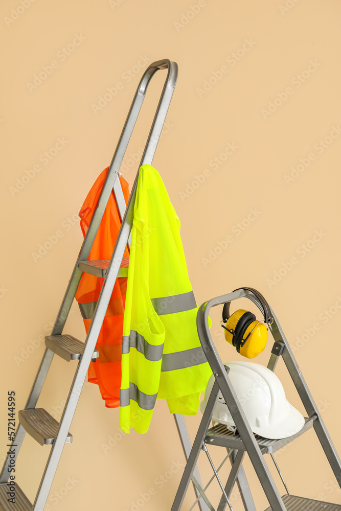Stepladders with builders equipment and reflective vests near beige wall
