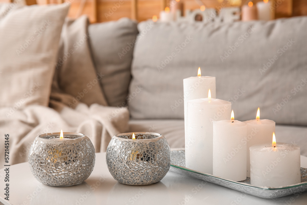 Holders with burning candles on table in living room, closeup