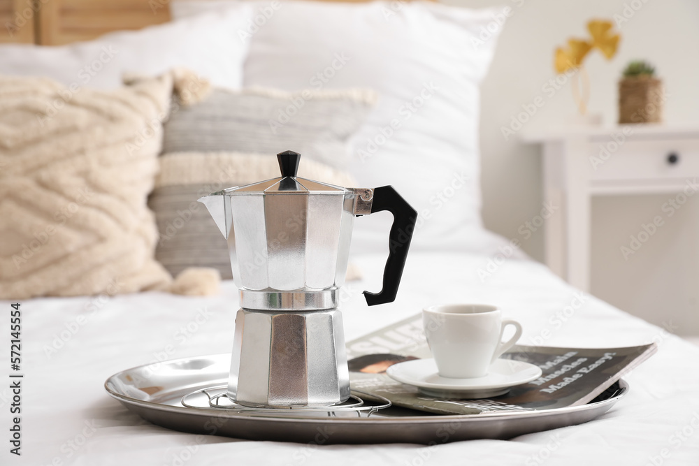 Tray with geyser coffee maker, cup of espresso and magazine on bed