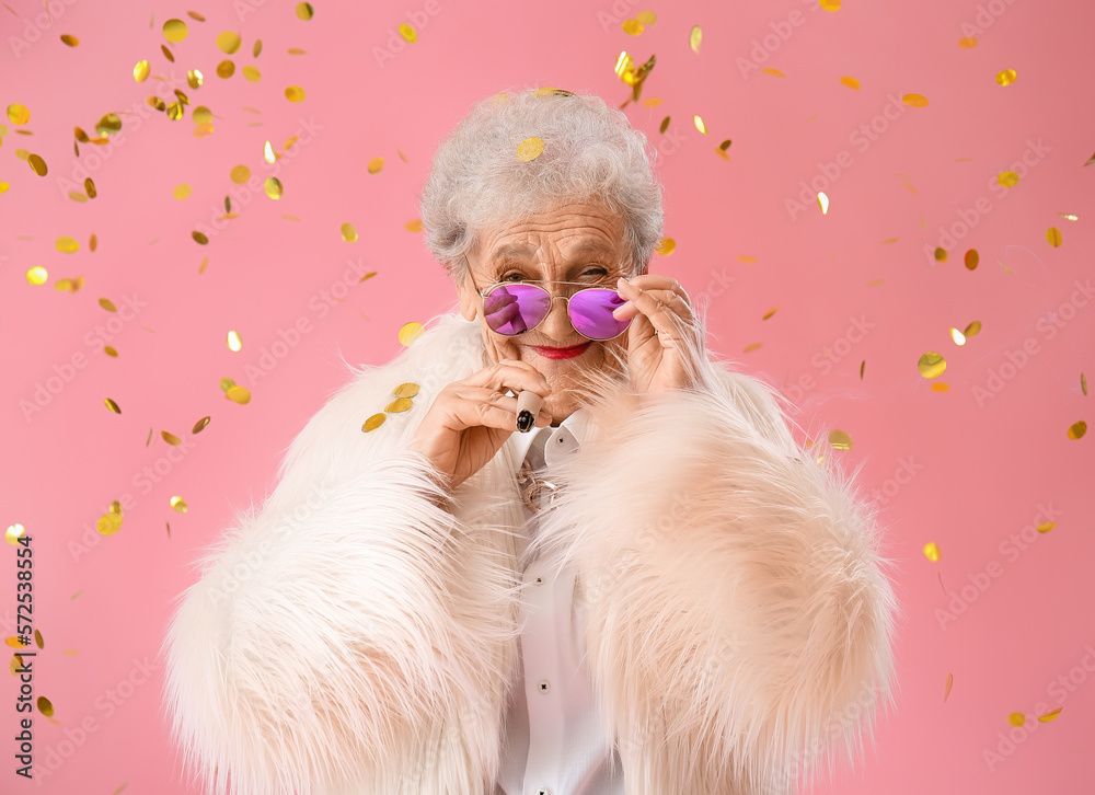 Senior woman in fur coat with cigarette and confetti on pink background