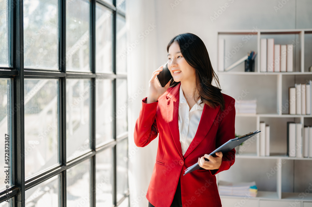 Business asian woman Talking on the phone and using a laptop with a smile while sitting at office