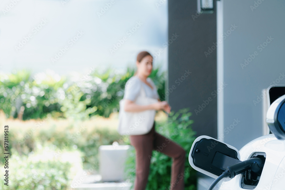 Focus EV charger plugged into EV car at home charging station with blurred background of progressive