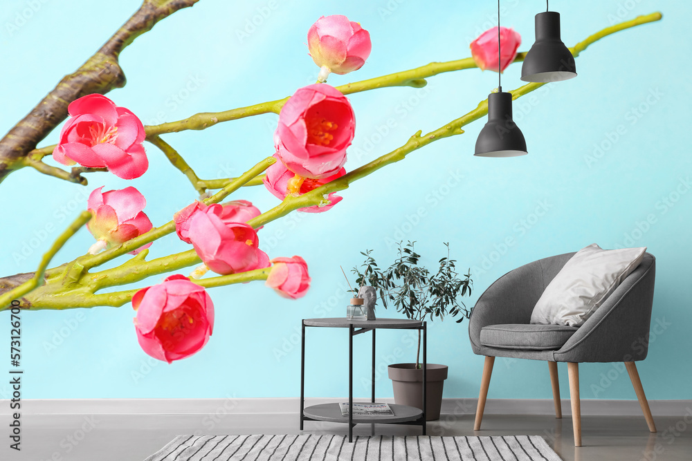 Grey armchair with table and houseplant near light blue wall with blooming Chinese plum branches in 