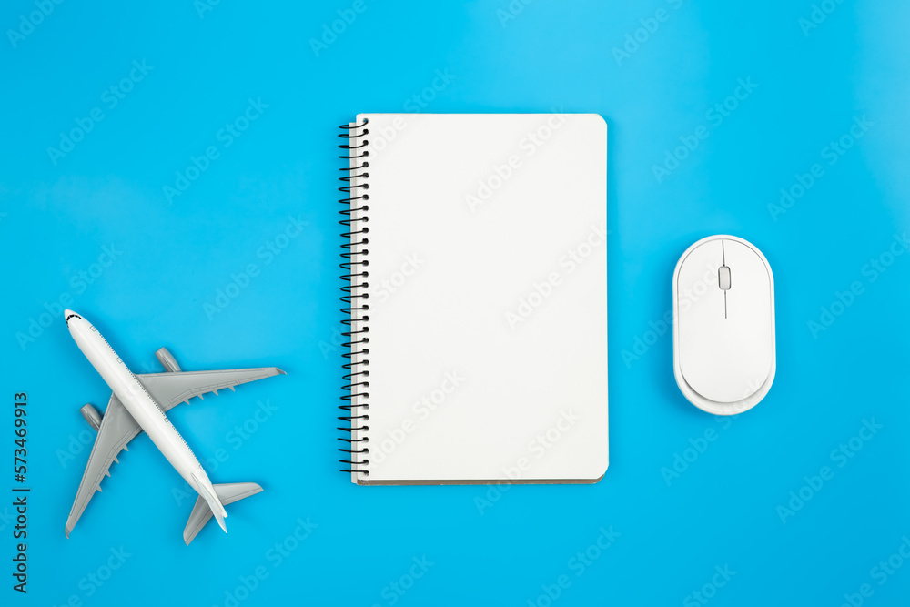 An airplane miniature, computer mouse and notebook on blue background, flat lay.