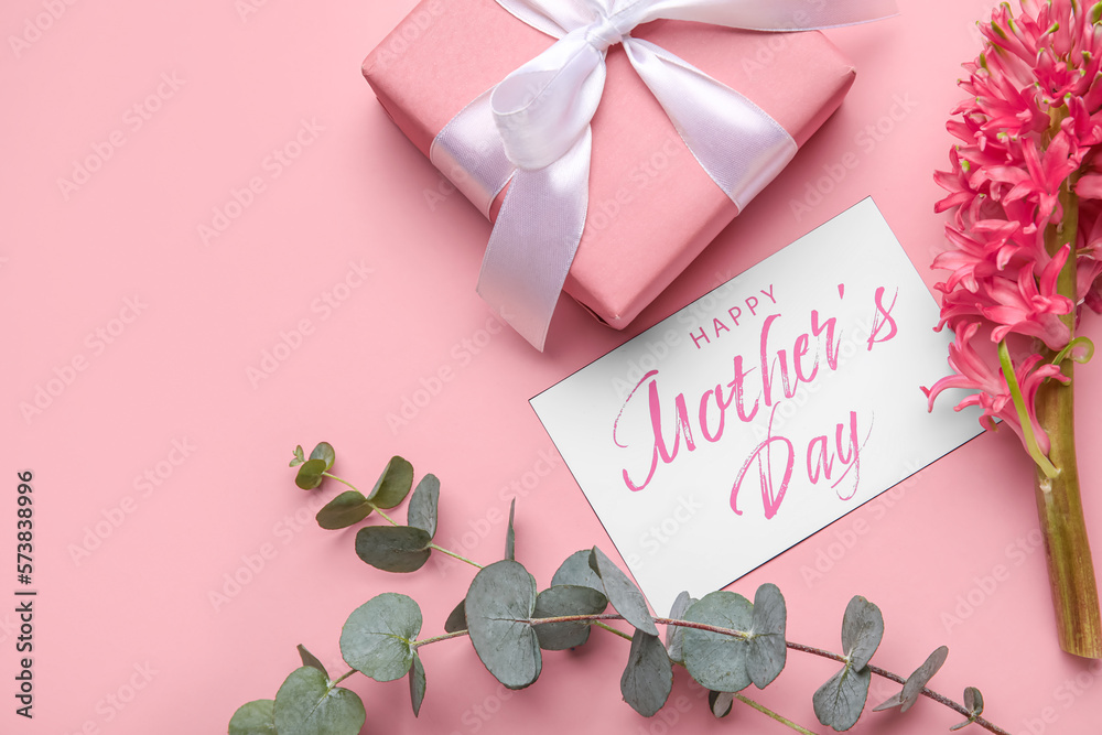 Card with text HAPPY MOTHERS DAY, eucalyptus branches, hyacinth flower and gift on pink background,