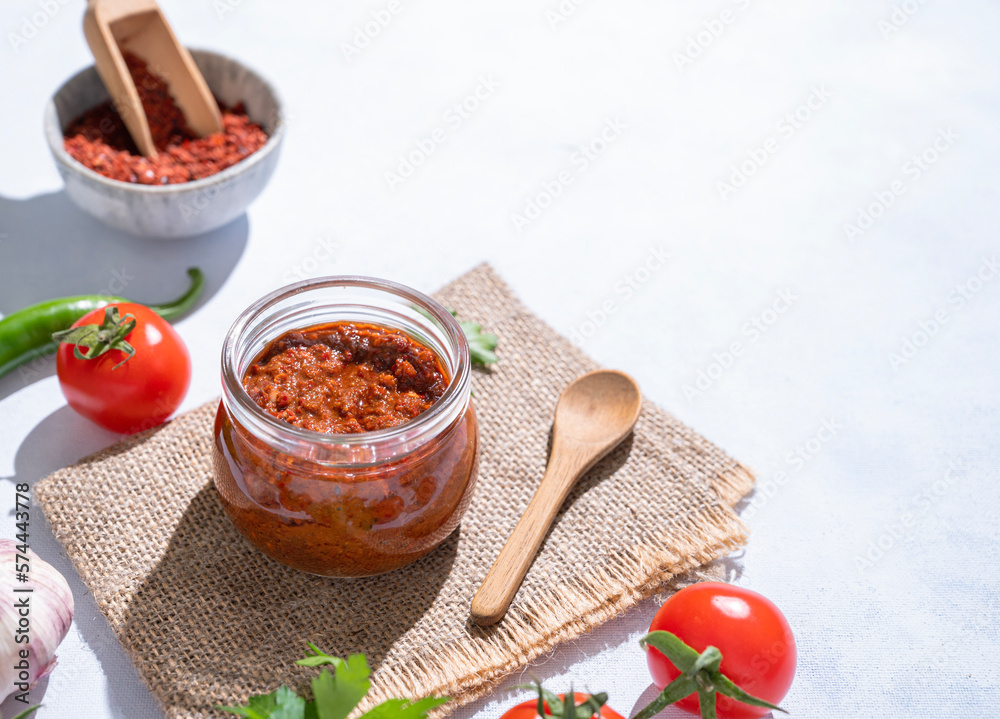 Homemade adjika sauce is an appetizer with tomatoes and hot peppers in a jar on a light background w