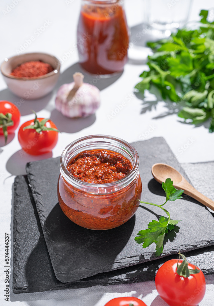 Homemade tomato sauce is an appetizer with tomatoes and hot peppers in a jar on a slate on a light b