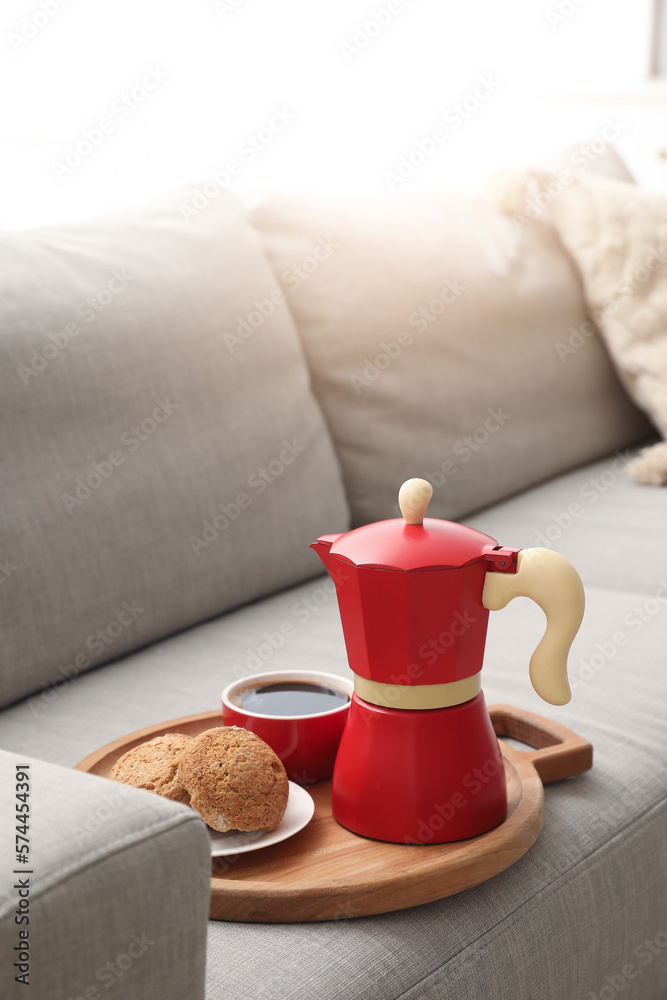 Board with geyser coffee maker, cup of espresso and cookies on sofa