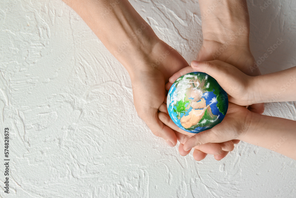 Hands of mother and child holding small planet Earth on white background