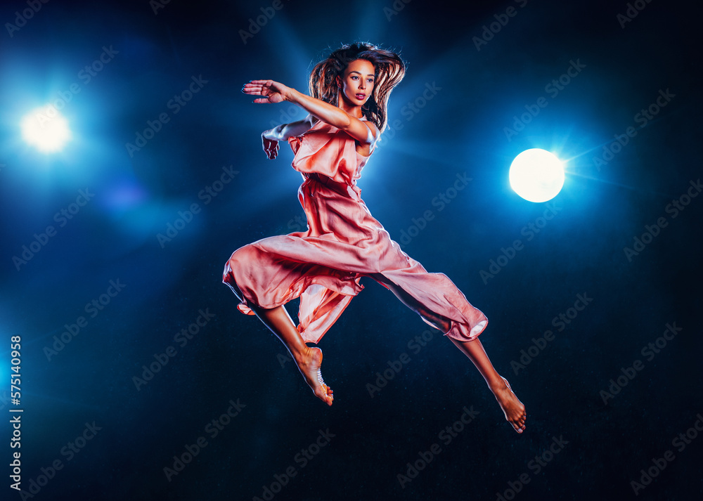 Young woman in pink dress jumping up on black background with lights