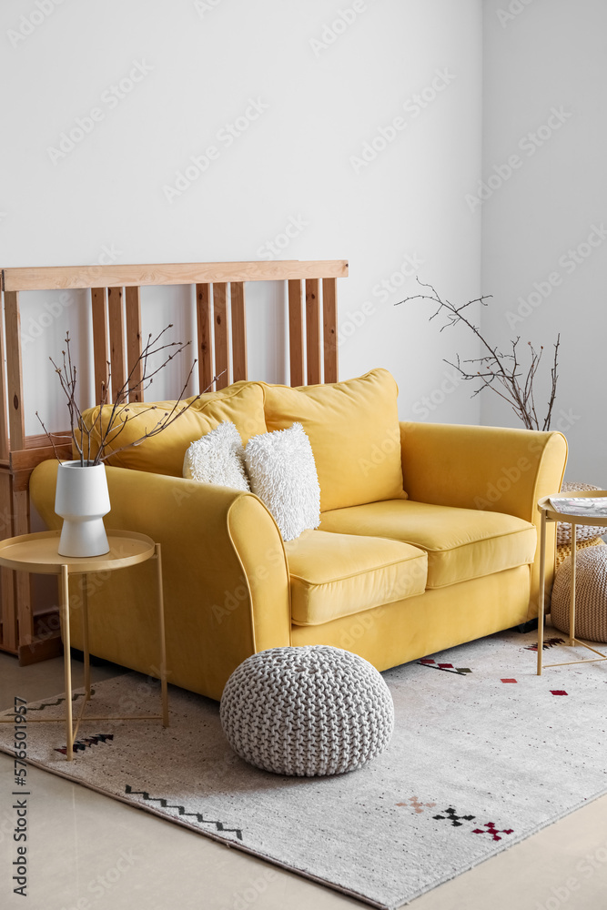 Interior of living room with yellow sofa and tree branches in vase