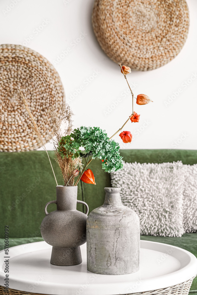 Vases with flowers on rattan table in living room